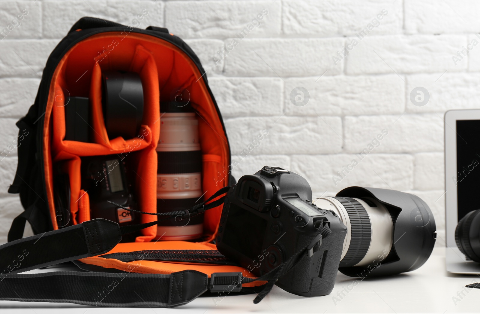 Photo of Camera and backpack with professional photographer's equipment on table indoors