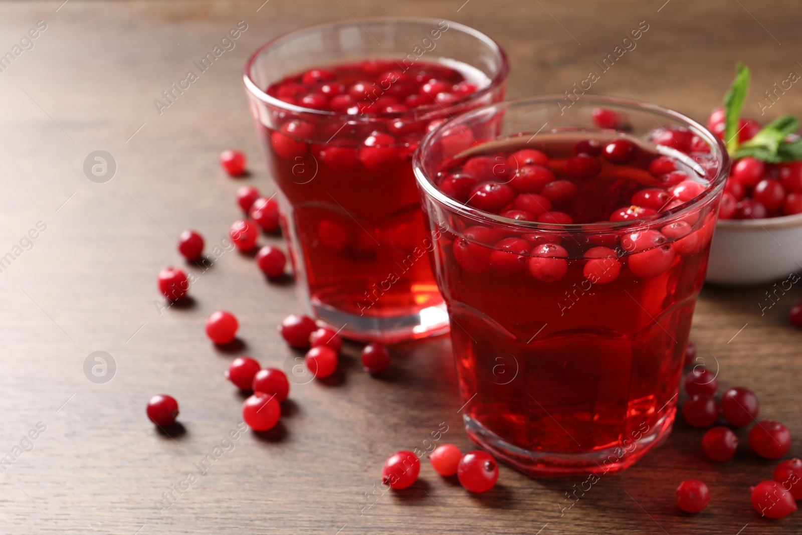 Photo of Tasty cranberry juice in glasses and fresh berries on wooden table, closeup. Space for text