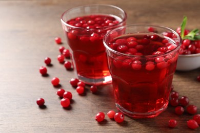 Tasty cranberry juice in glasses and fresh berries on wooden table, closeup. Space for text