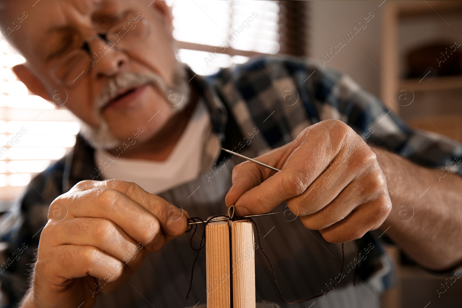 Photo of Man sewing piece of leather in workshop, closeup