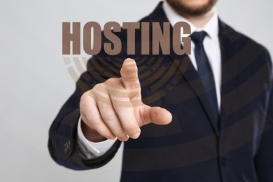 Image of Businessman pointing at word HOSTING on virtual screen against light background, focus on hand