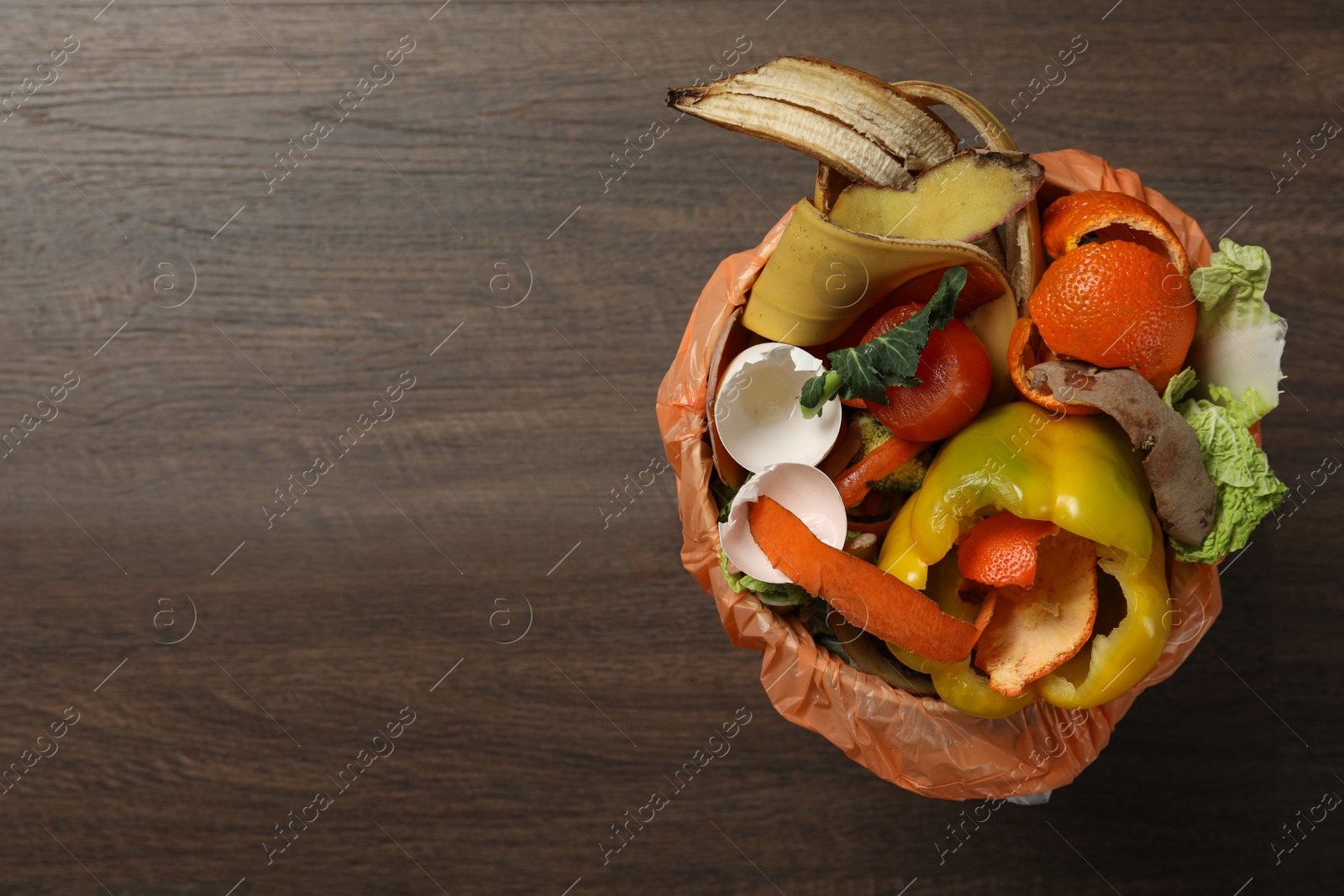 Photo of Natural garbage in trash bin on wooden background, top view with space for text. Composting of organic waste