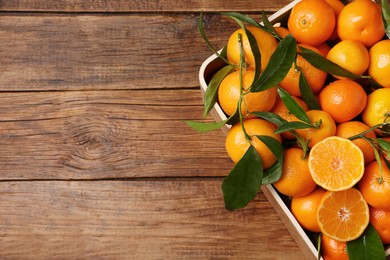 Photo of Fresh tangerines with green leaves in crate on wooden table, top view. Space for text