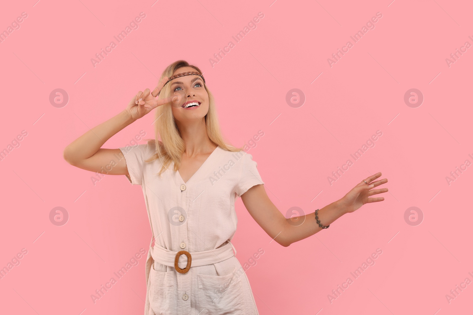 Photo of Portrait of smiling hippie woman showing peace sign on pink background