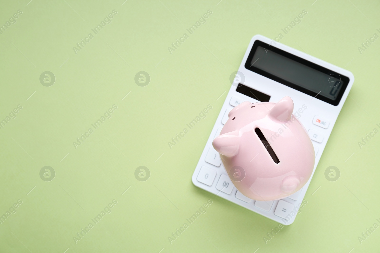 Photo of Piggy bank and calculator on light green background, top view. Space for text