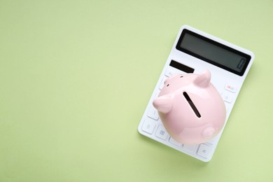 Piggy bank and calculator on light green background, top view. Space for text