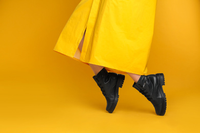 Photo of Woman wearing stylish boots on yellow background, closeup