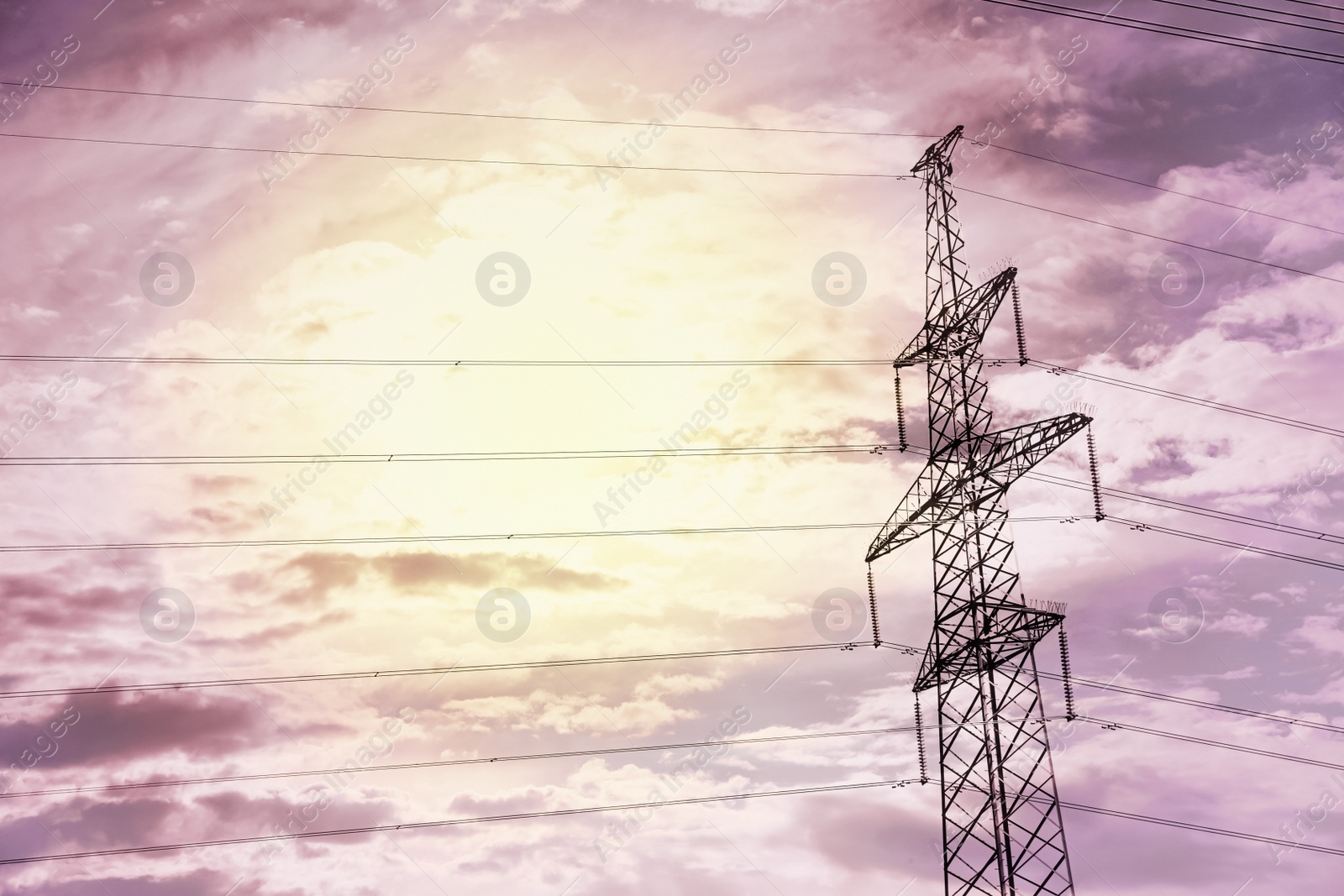 Photo of High voltage tower with electricity transmission power lines at sunset, low angle view