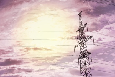 Photo of High voltage tower with electricity transmission power lines at sunset, low angle view