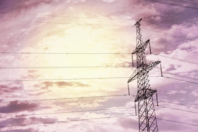 High voltage tower with electricity transmission power lines at sunset, low angle view