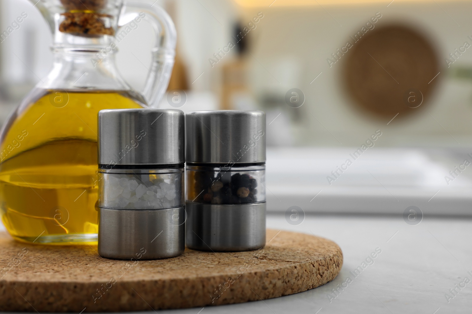 Photo of Salt and pepper mills with bottle of oil on table in kitchen. Space for text