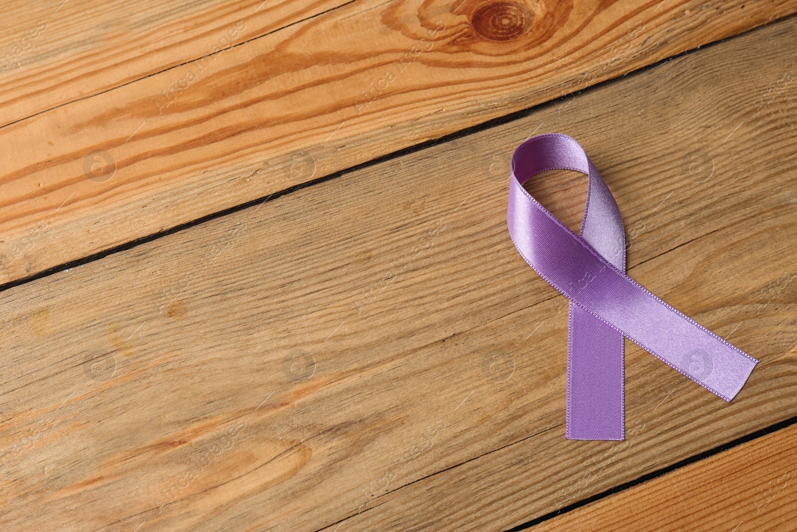 Photo of Purple ribbon on brown wooden background, space for text. Domestic violence awareness