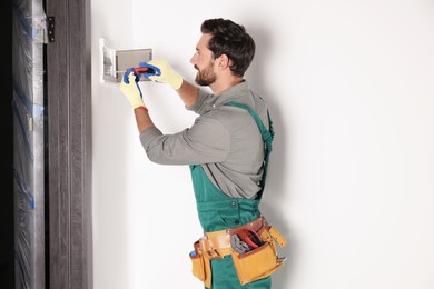 Electrician installing fuse box with screwdriver indoors