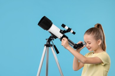 Happy girl looking at stars through telescope on light blue background, space for text