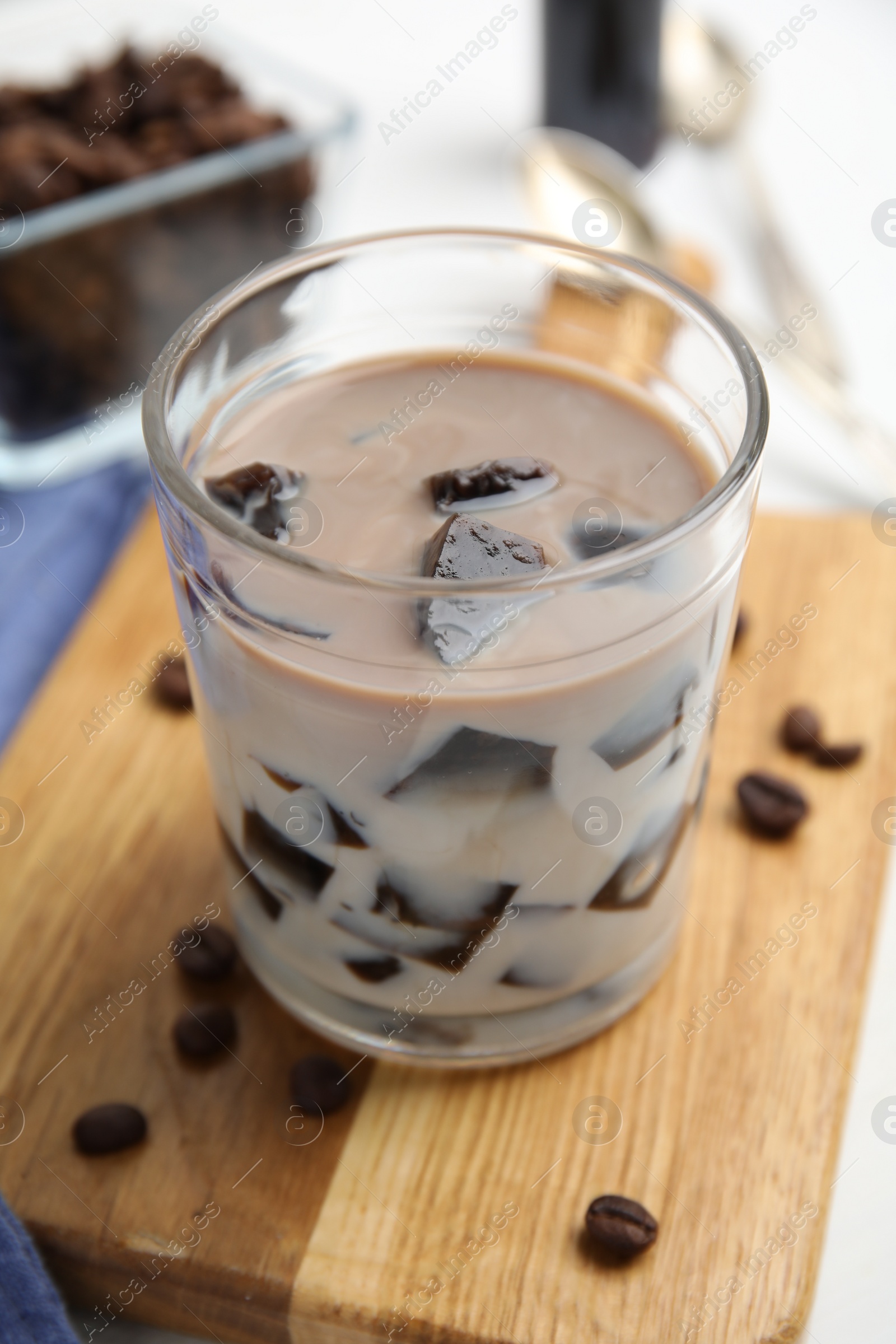 Photo of Glass of milk with grass jelly and coffee beans on wooden board, closeup