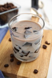 Photo of Glass of milk with grass jelly and coffee beans on wooden board, closeup