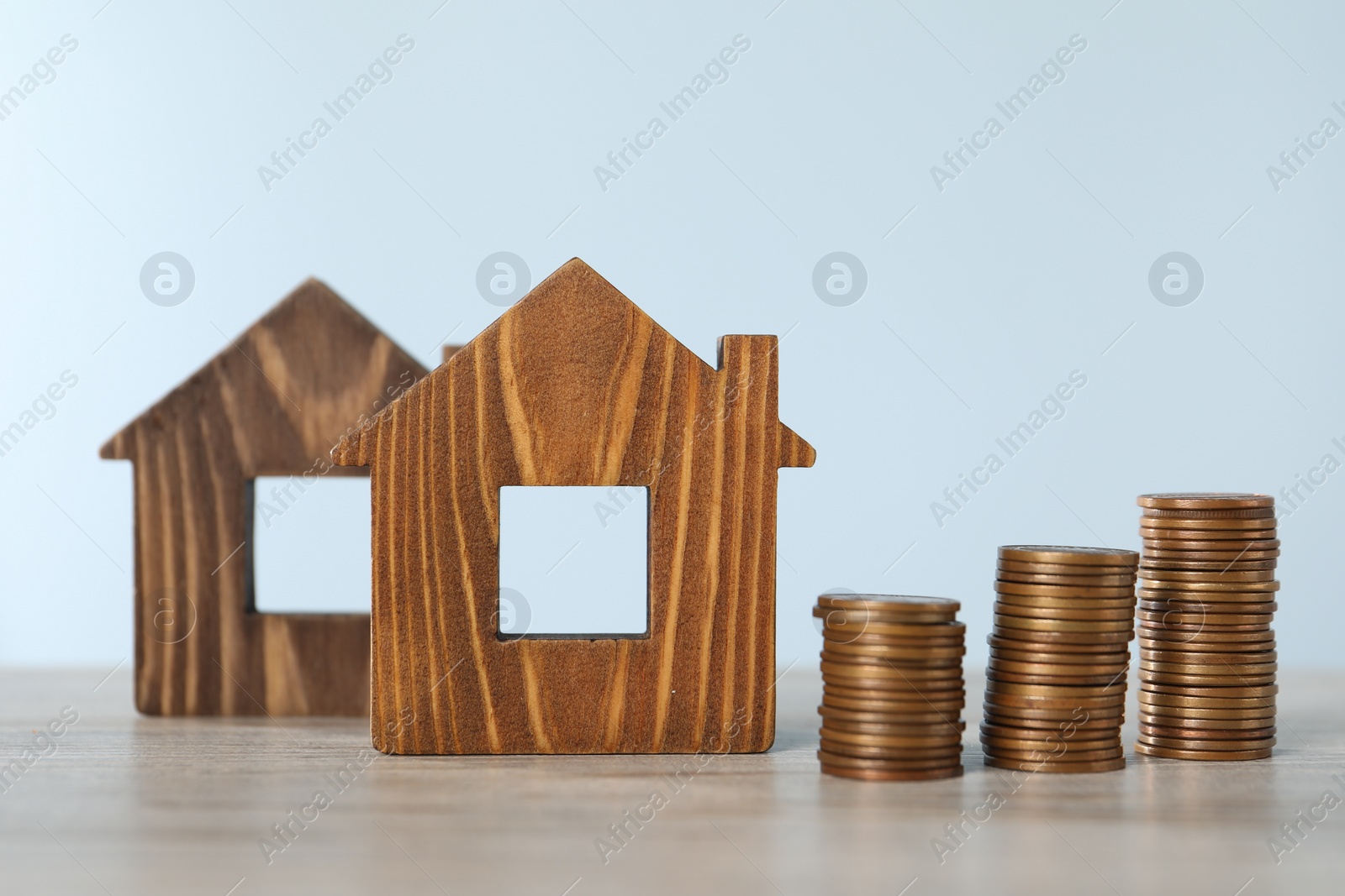 Photo of House models and stacked coins on wooden table against light blue background