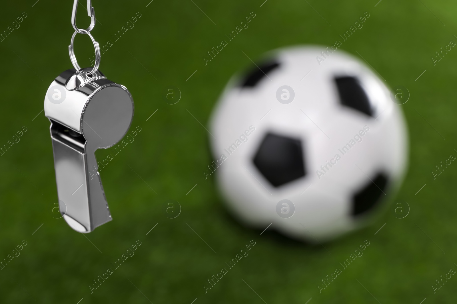 Photo of Football referee equipment. Metal whistle and soccer ball on green grass, closeup with space for text