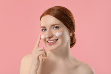 Photo of Smiling woman with freckles and cream on her face against pink background