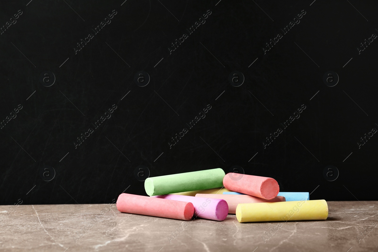 Photo of Color pieces of chalk on table near blackboard