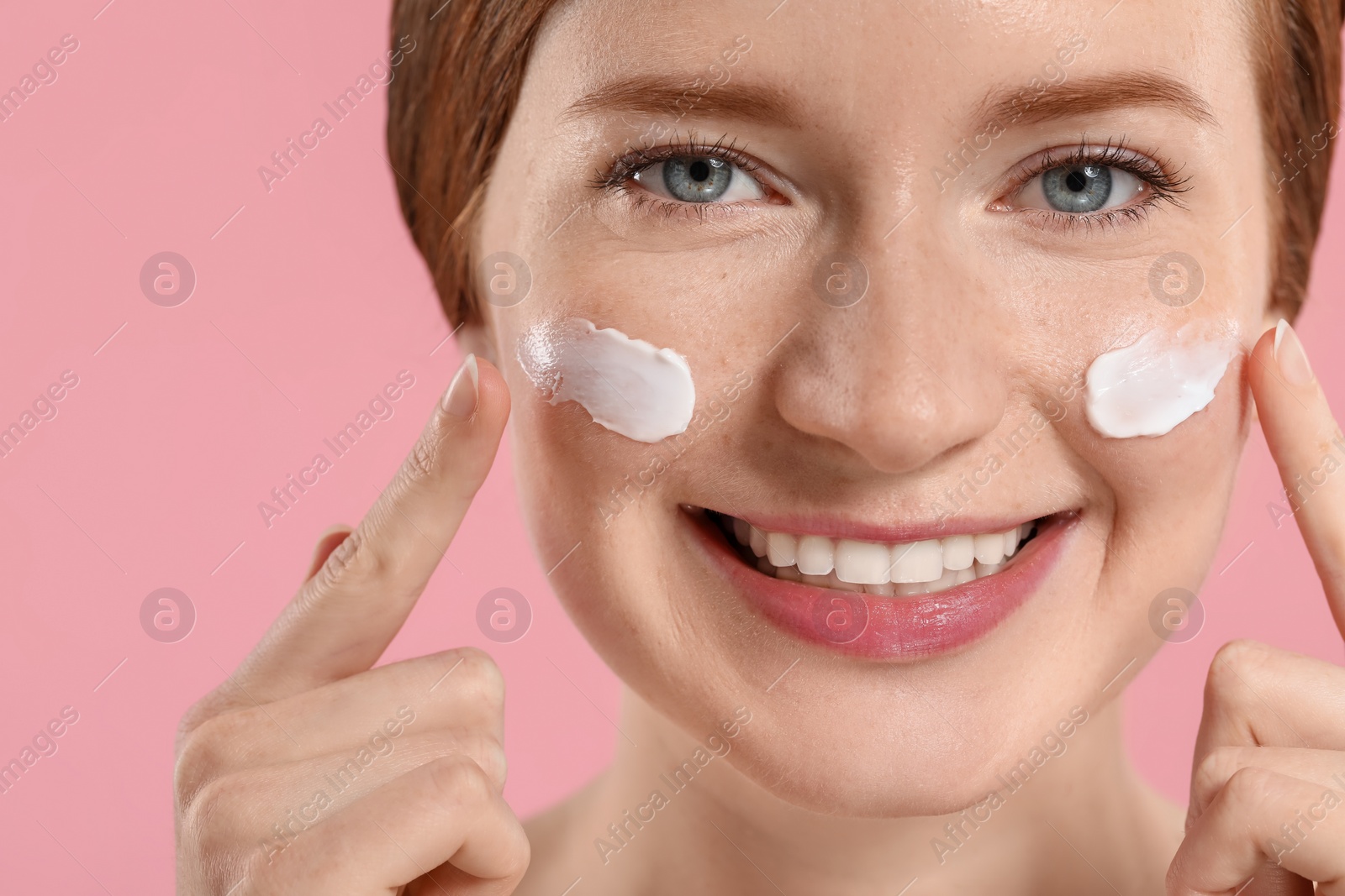 Photo of Smiling woman with freckles and cream on her face against pink background, closeup