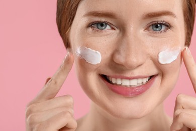 Photo of Smiling woman with freckles and cream on her face against pink background, closeup