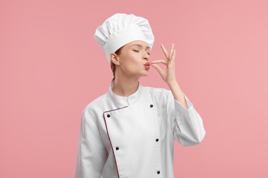 Young woman chef in uniform showing perfect sign on pink background