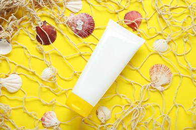 Photo of Tube of suntan cream, seashells and net on yellow background, flat lay