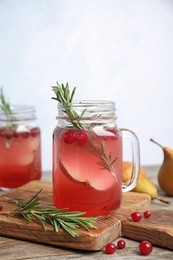 Photo of Tasty refreshing cranberry cocktail with rosemary in mason jars on table