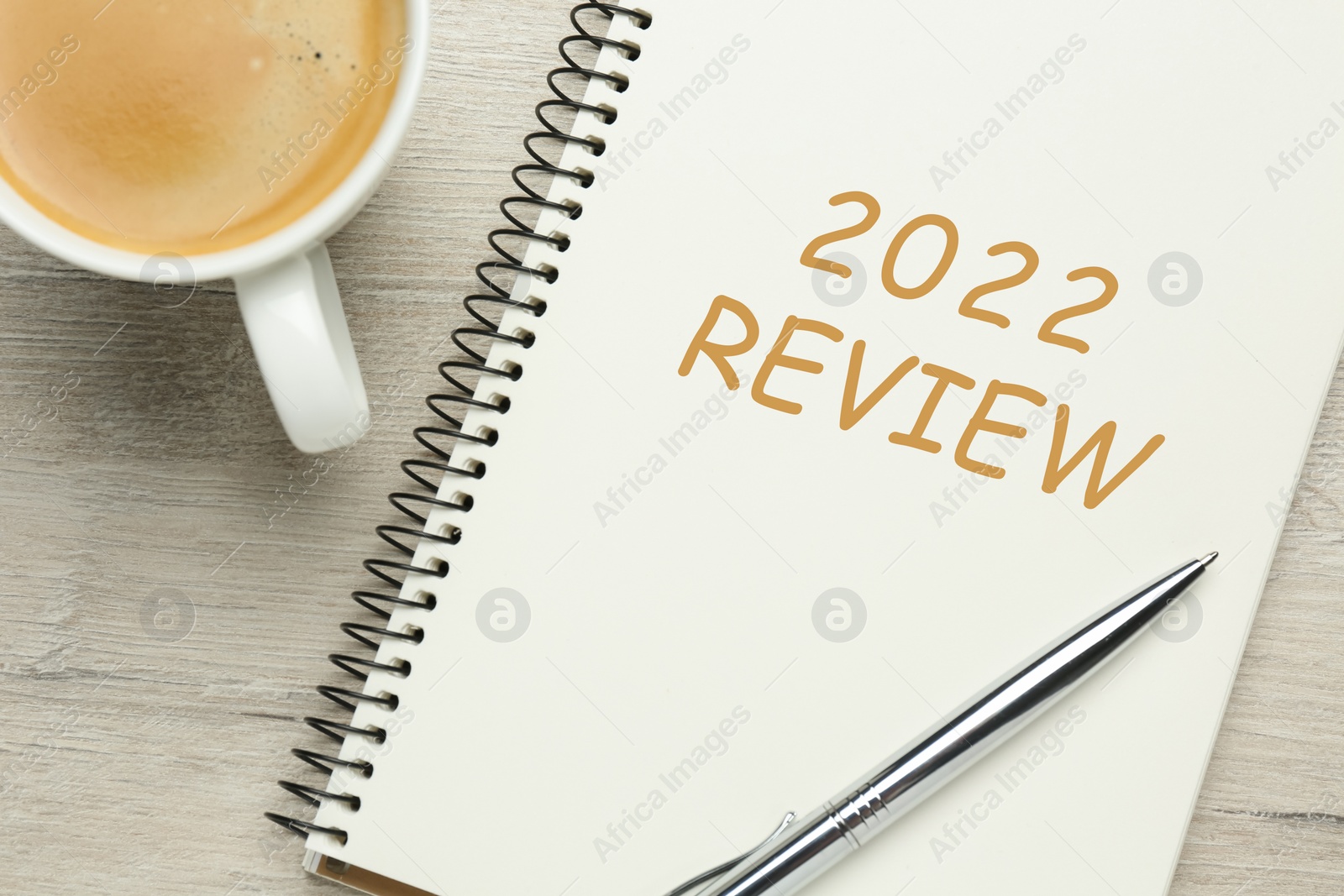 Image of Text 2022 Review written in notebook, pen and cup of coffee on wooden table, top view