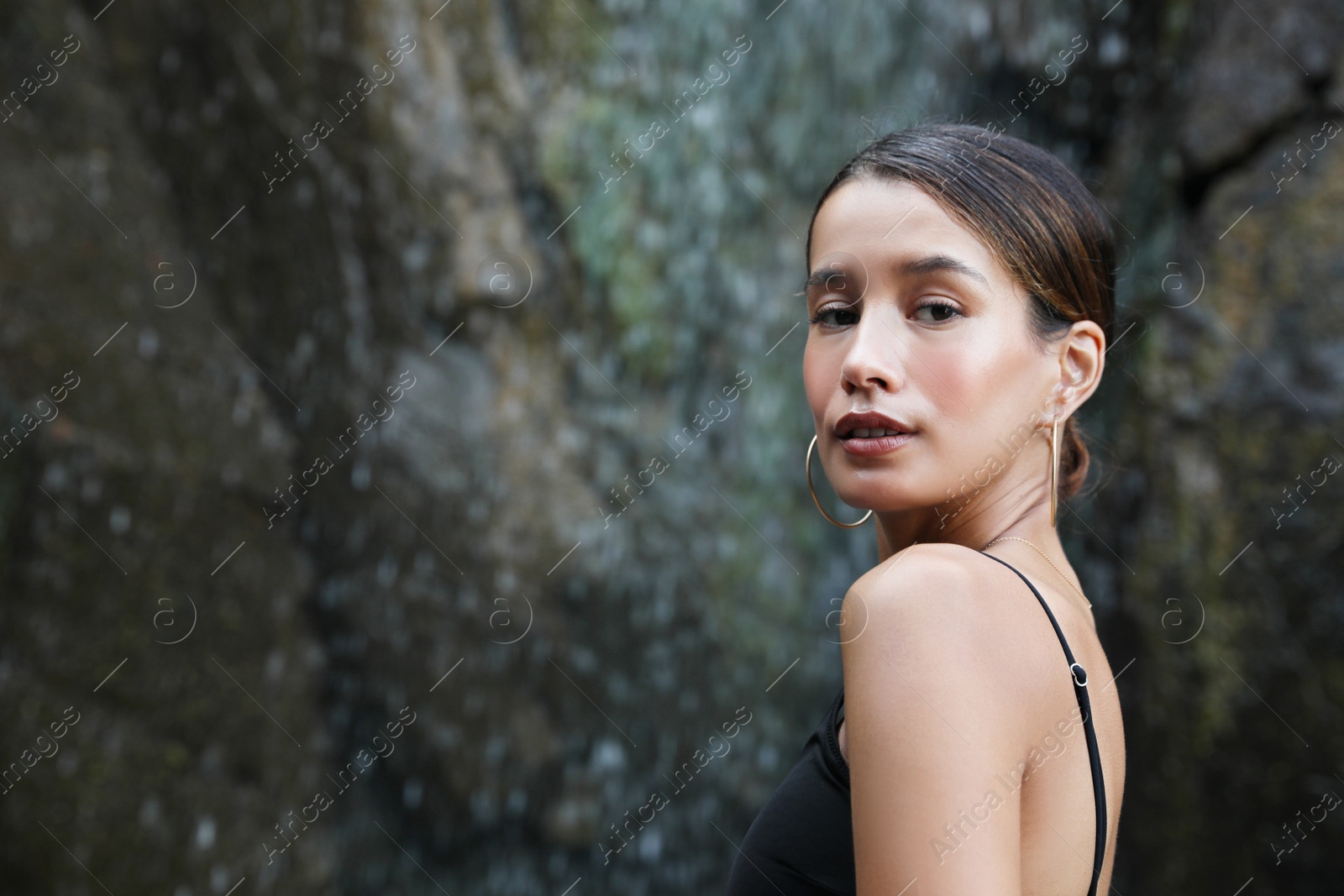 Photo of Beautiful young woman in stylish bikini near waterfall outdoors, space for text