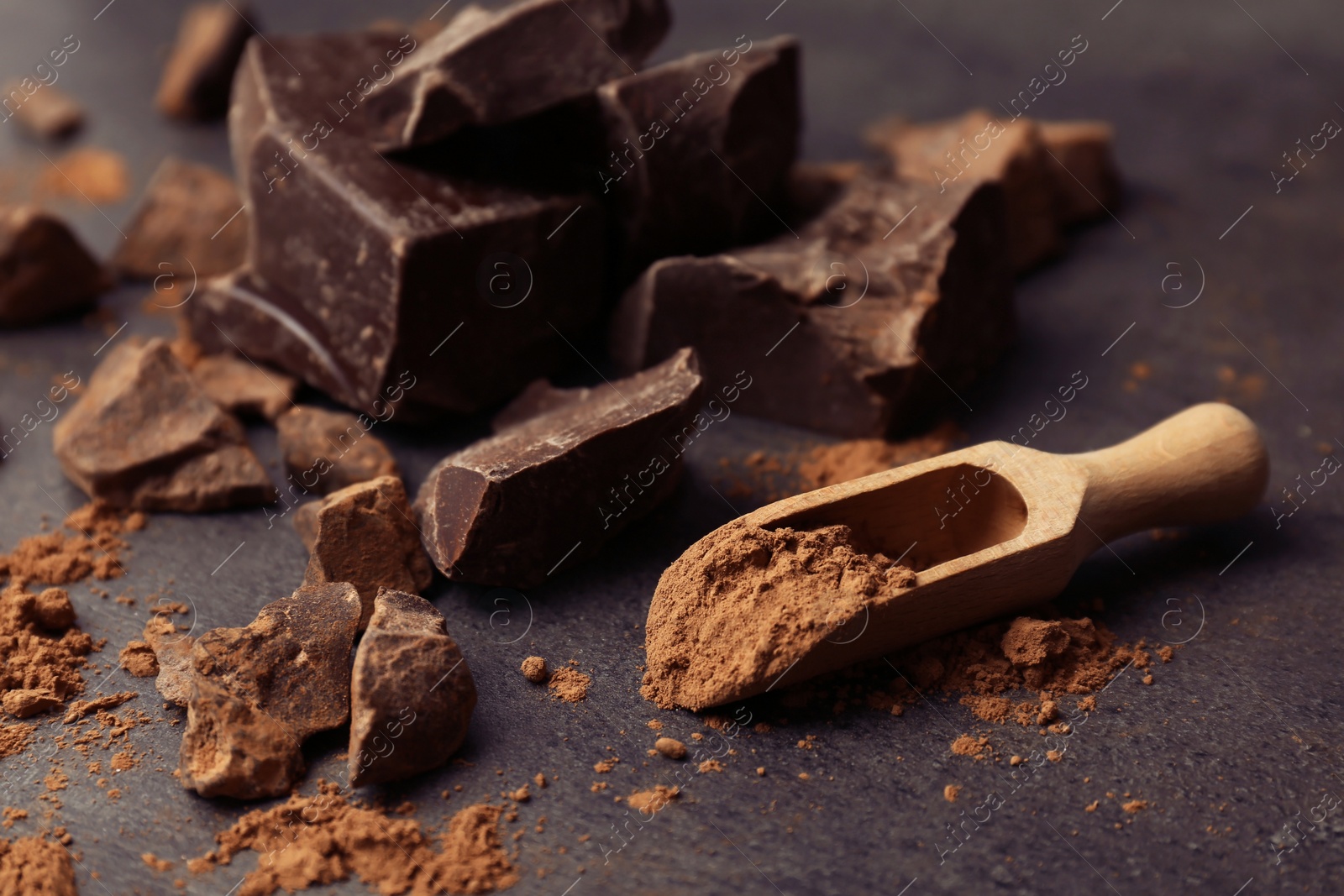 Photo of Scoop with cocoa powder and tasty chocolate on dark table