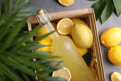 Photo of Tasty limoncello liqueur, lemons and green leaves on grey table, flat lay