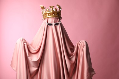 Photo of Glamorous ghost. Woman in sheet with sunglasses and crown on pink background