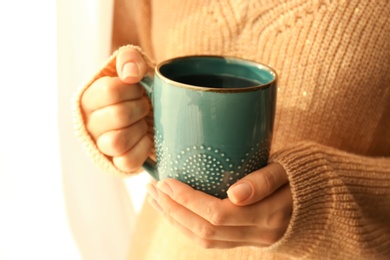 Woman holding elegant cup with tea near window indoors, closeup