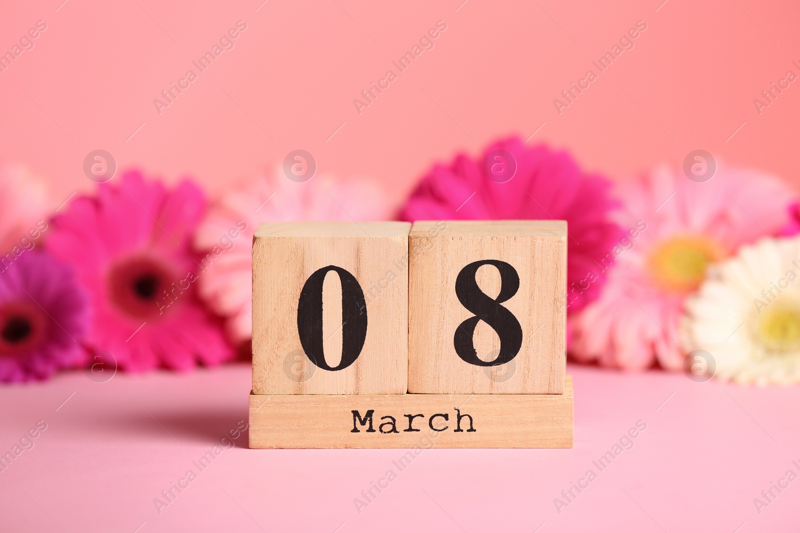 Photo of Wooden block calendar and flowers on table against color background. International Women's Day