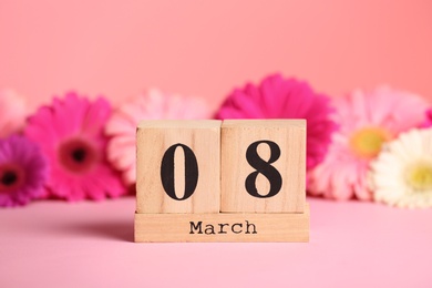 Photo of Wooden block calendar and flowers on table against color background. International Women's Day