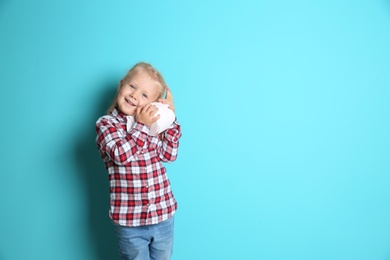 Cute little girl holding toilet paper roll on color background. Space for text