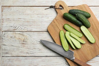 Photo of Whole and cut fresh ripe cucumbers on white wooden table, flat lay. Space for text