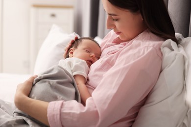 Mother with her sleeping newborn baby in bed at home