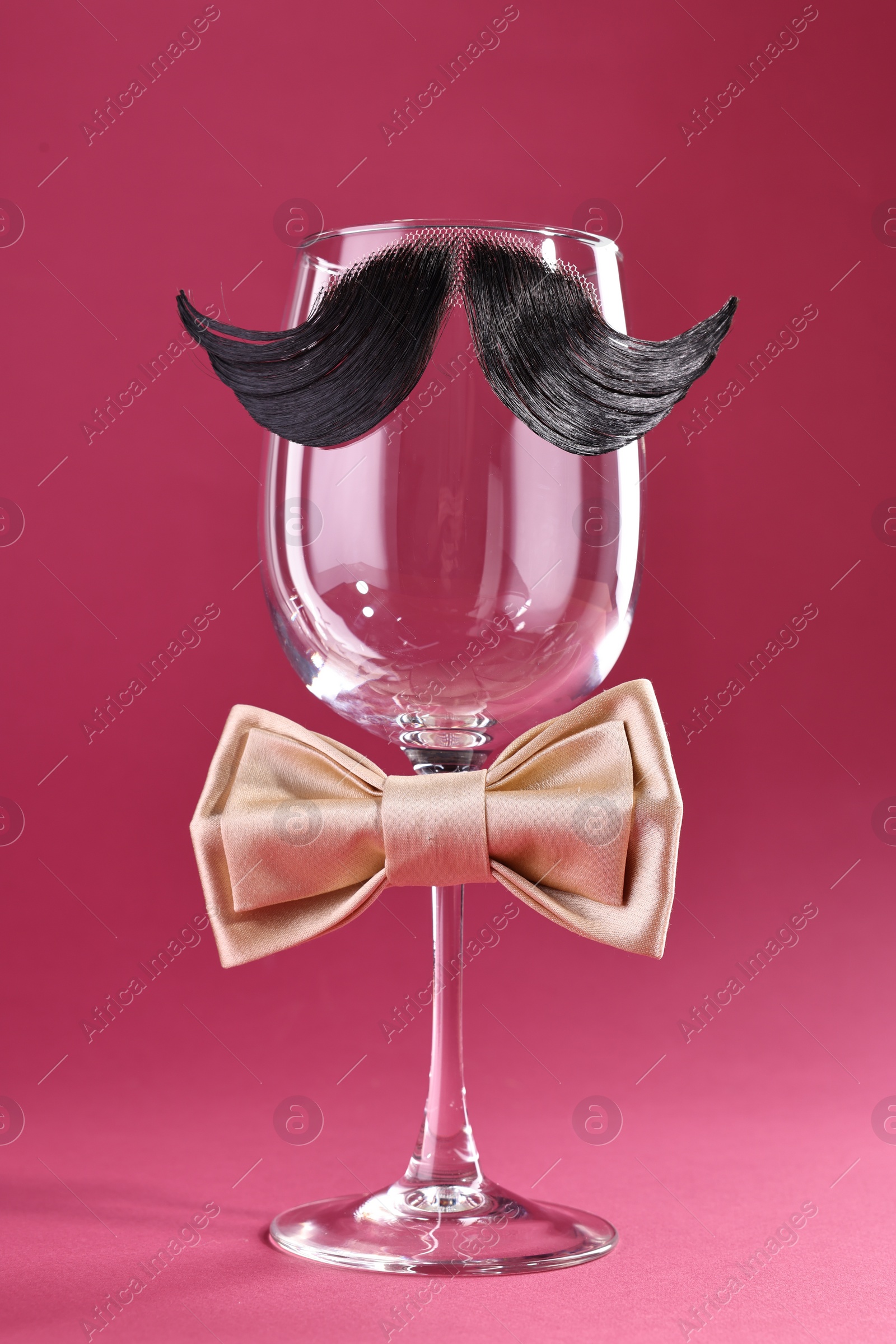 Photo of Man's face made of artificial mustache, bow tie and wine glass on crimson background