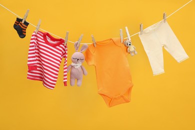 Photo of Different baby clothes and toys drying on laundry line against orange background