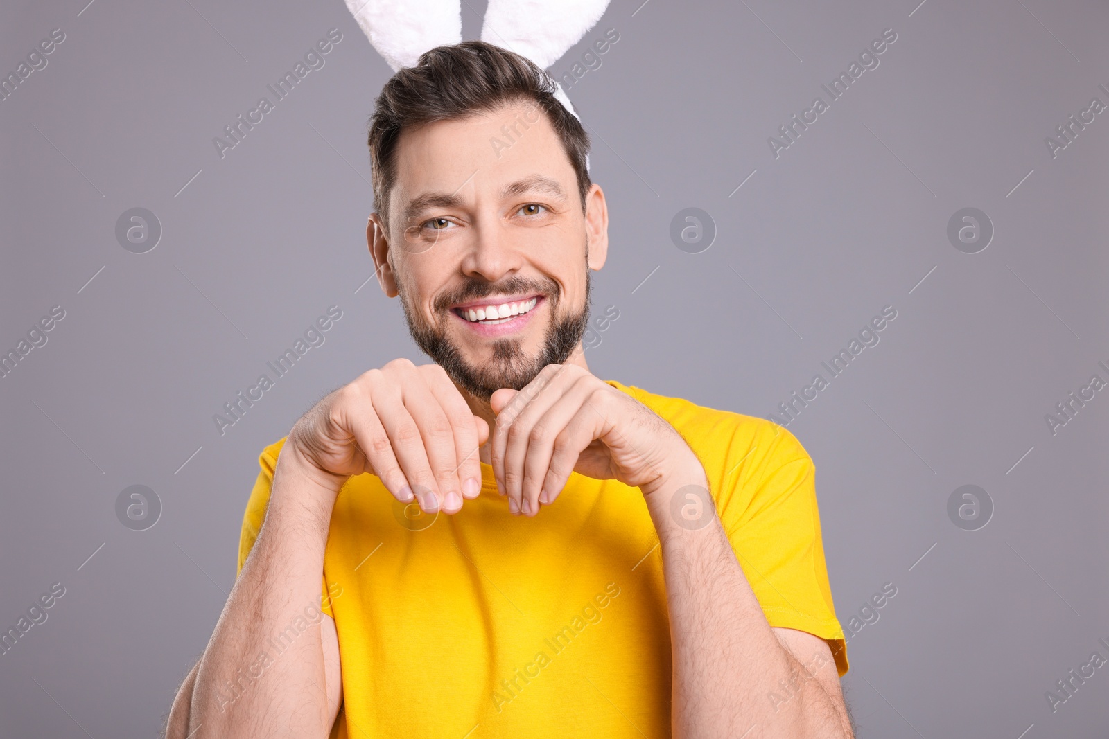 Photo of Happy man wearing bunny ears headband on grey background. Easter celebration