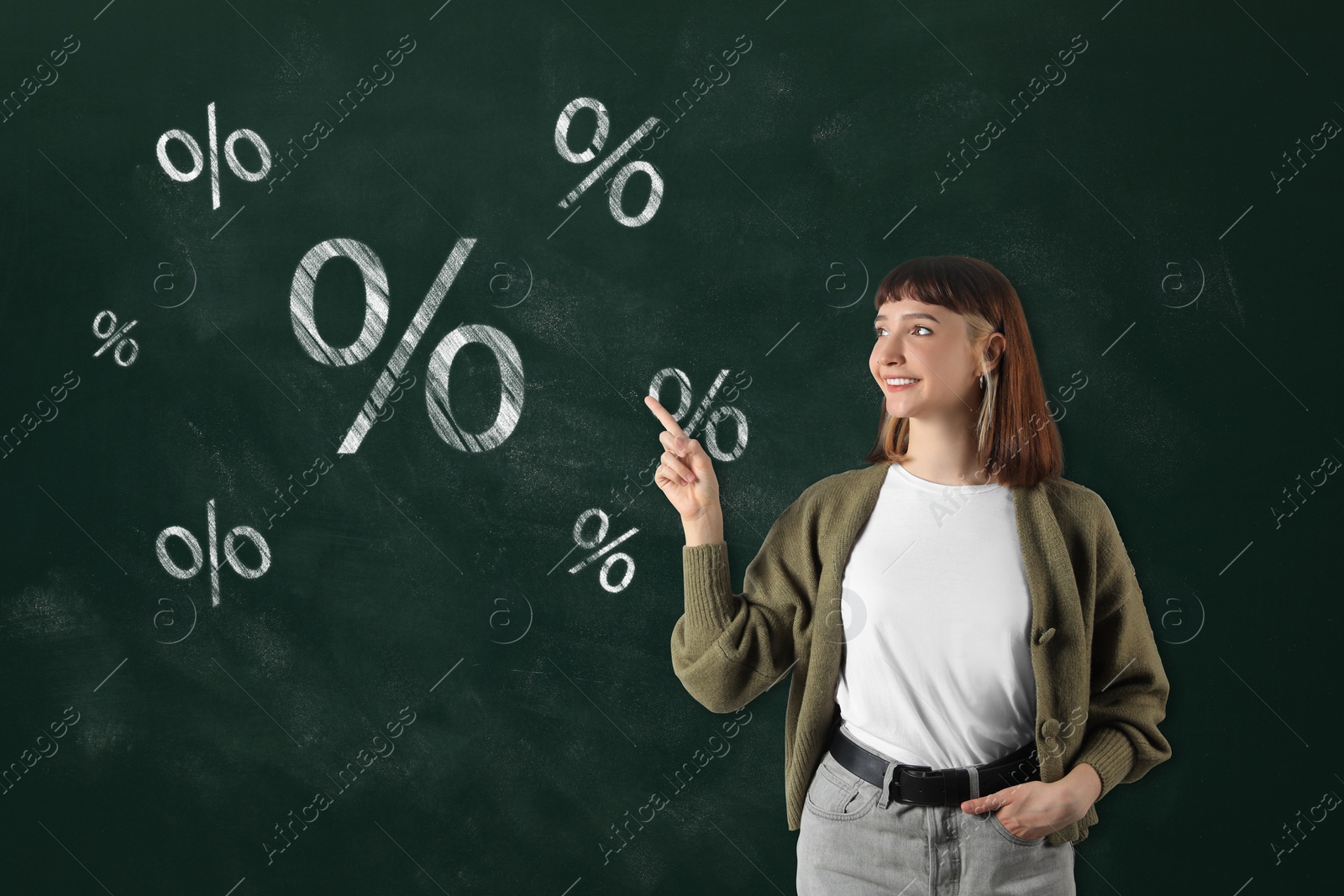 Image of Discount offer. Happy woman pointing at drawn on green chalkboard percent signs