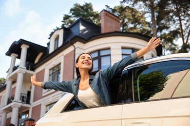 Enjoying trip. Happy young woman leaning out of car window on city street, low angle view