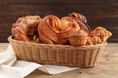 Wicker basket with different tasty freshly baked pastries on wooden table