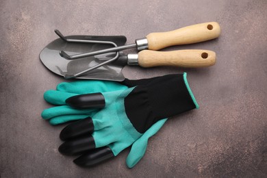 Photo of Claw gardening gloves, trowel and rake on brown textured table, top view