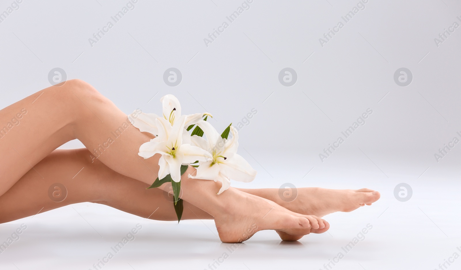 Photo of Young woman with silky skin and flowers on light background, closeup of legs