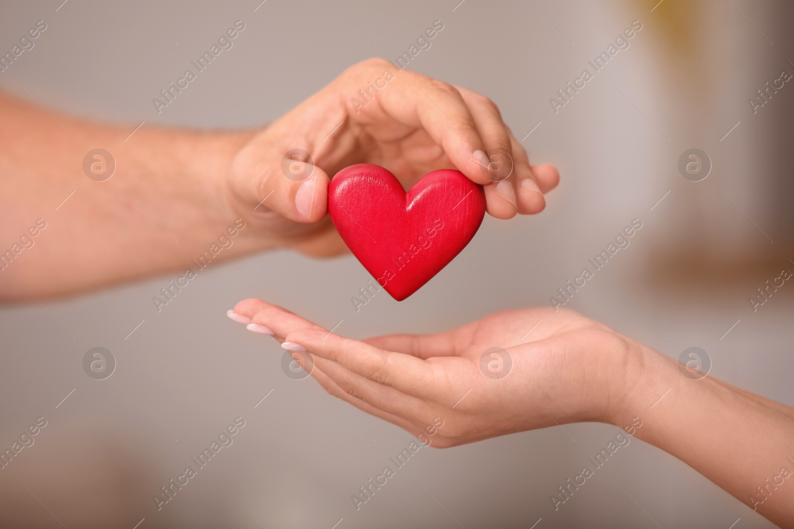 Photo of Man giving red heart to woman on blurred background, closeup. Donation concept