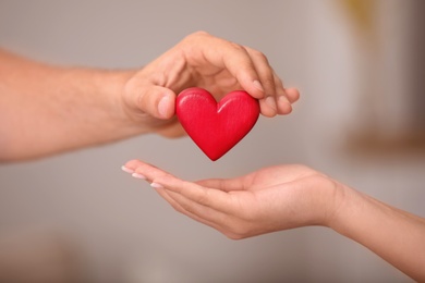 Man giving red heart to woman on blurred background, closeup. Donation concept